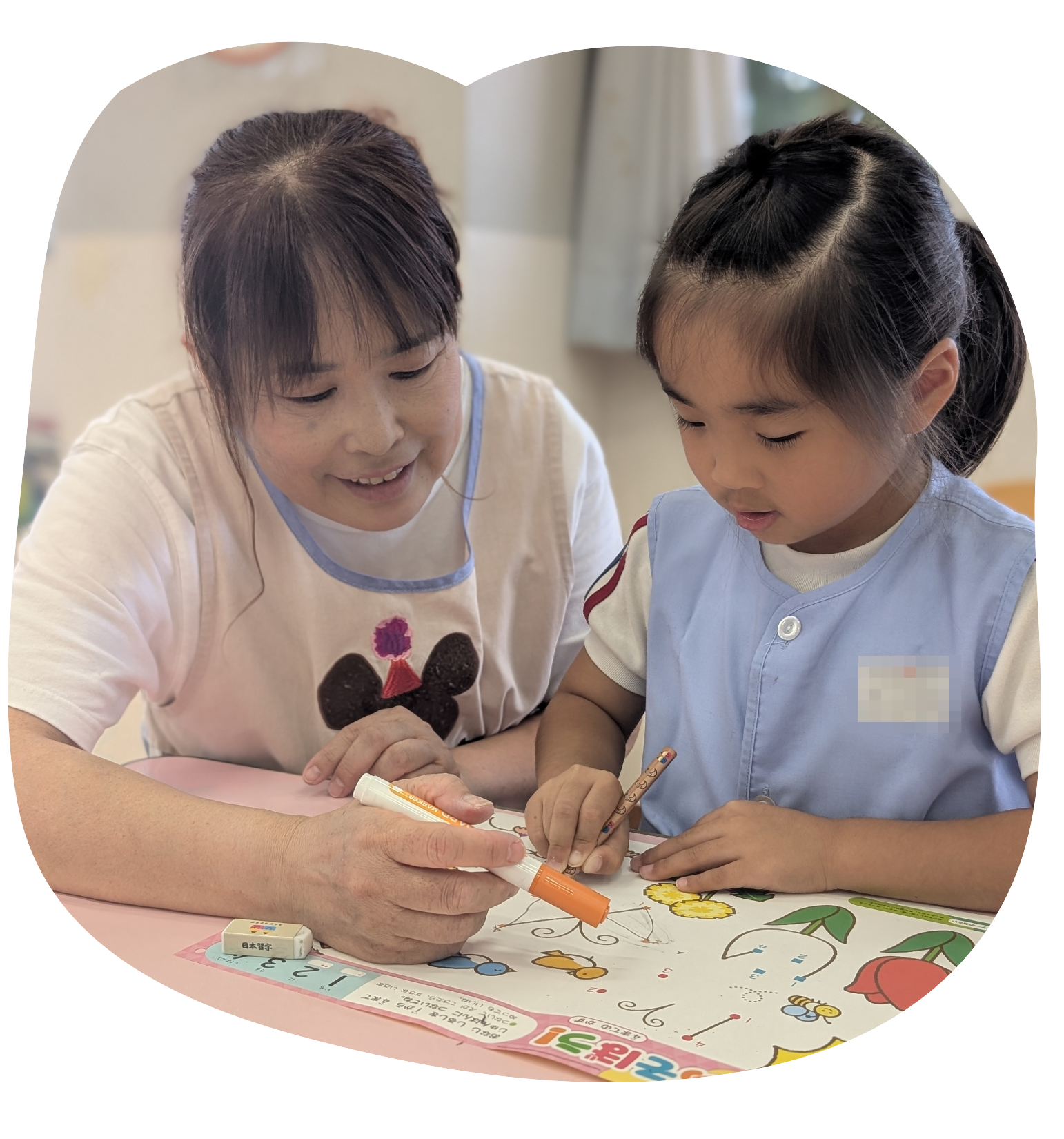 先生と女の子が一緒に書き方の練習をする様子
