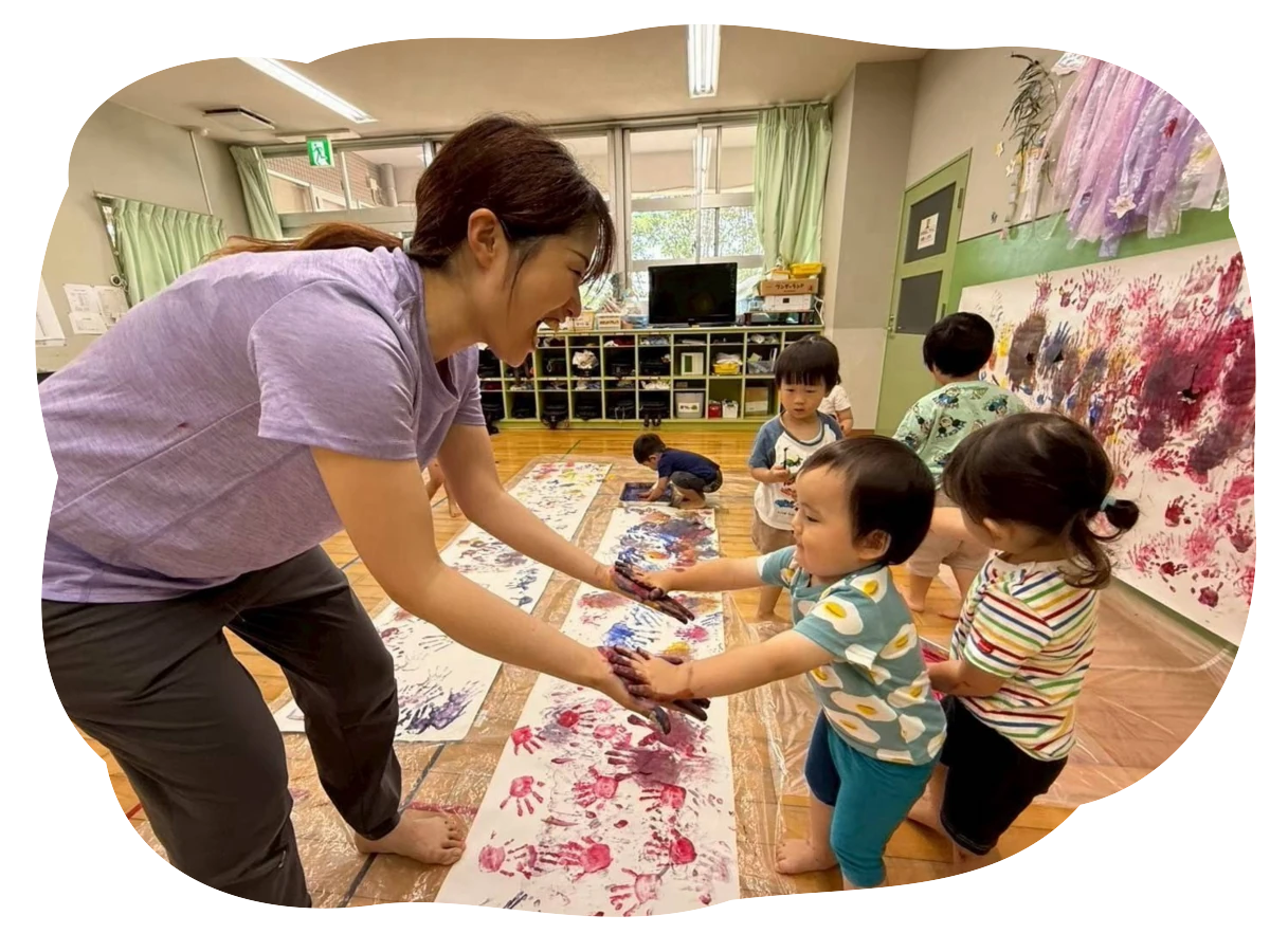 先生と園児が手形絵の具遊びを楽しんでいる様子